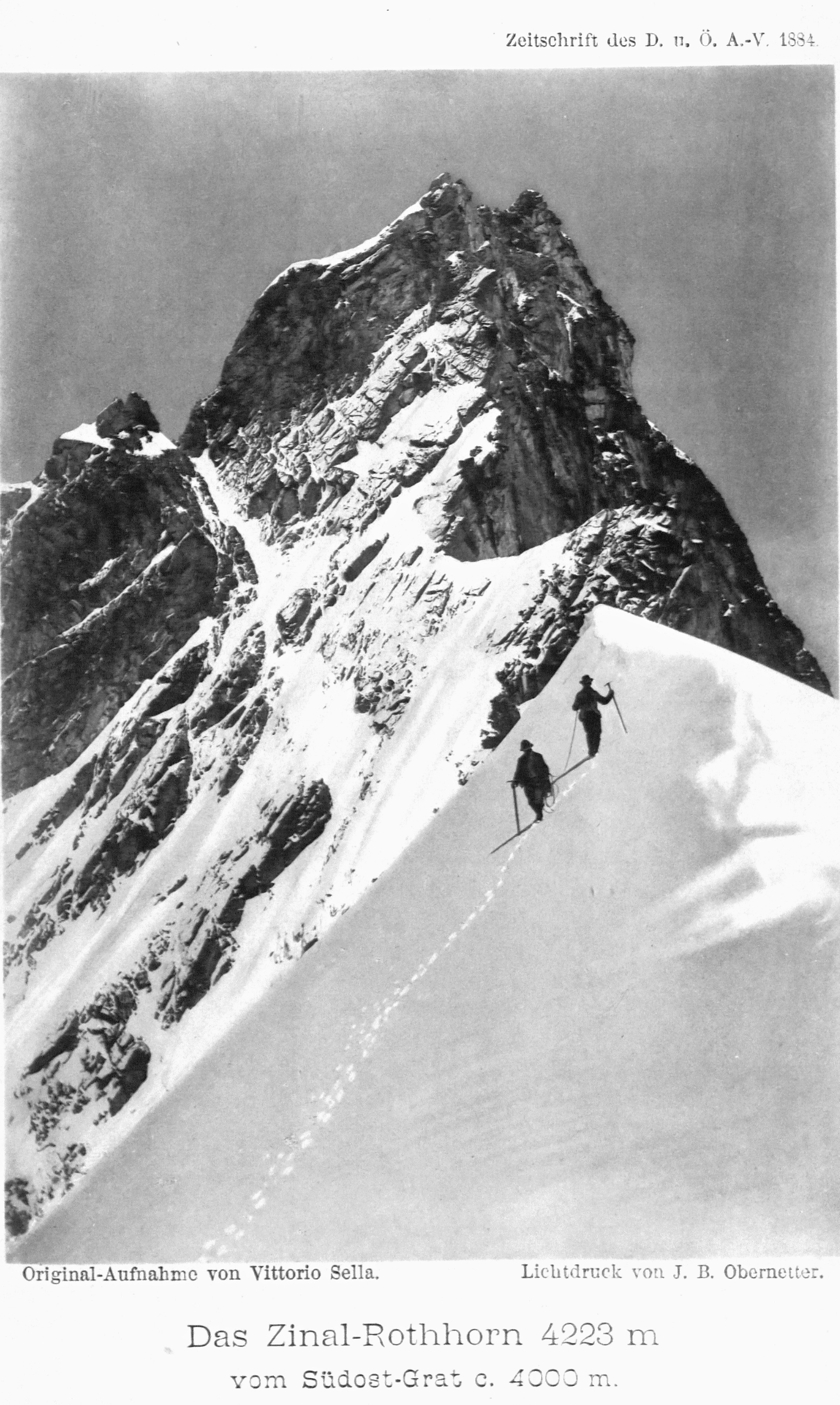 A tall black-and-white mountain photograph. Two small roped figures with long ice axes climb a sunlit snow crest that runs from the lower left to the upper right. Their boot track descends behind them as a dotted line across a snow field that carries no other texture. Down the left margin, broken rock ribs run almost to the bottom edge. Above and to the left, a dark but fully modelled rock pyramid, its strata and snow ledges legible throughout, rises against an even, structureless sky. Printed captions in German appear below the picture.